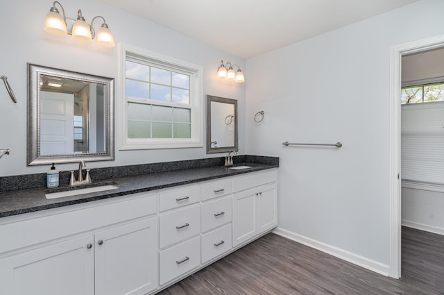full bath with a sink, baseboards, double vanity, and wood finished floors