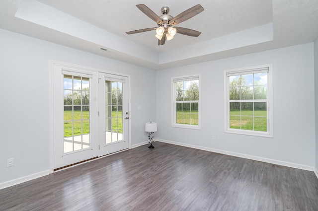 empty room with dark wood-type flooring, a tray ceiling, and baseboards