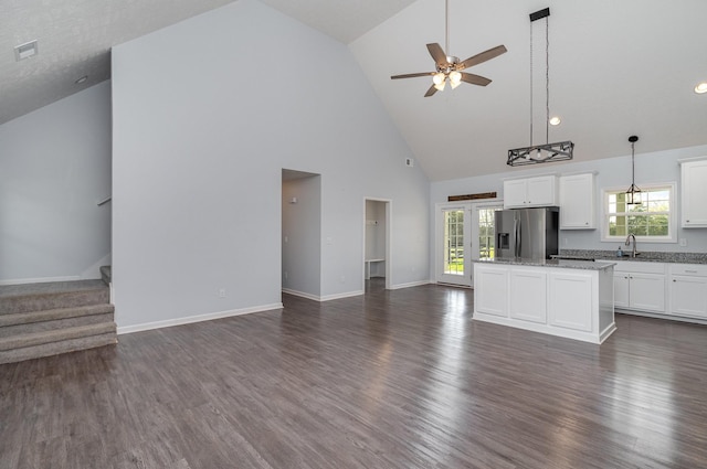 unfurnished living room with high vaulted ceiling, a ceiling fan, dark wood-style flooring, stairs, and baseboards