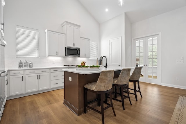 kitchen with a kitchen island with sink, light wood-style flooring, stainless steel microwave, a kitchen breakfast bar, and light countertops