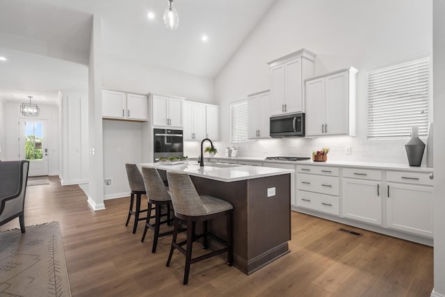 kitchen featuring wood finished floors, a kitchen island with sink, a sink, stainless steel appliances, and white cabinetry