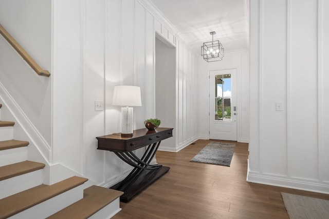 entrance foyer featuring ornamental molding, dark wood finished floors, stairway, an inviting chandelier, and a decorative wall