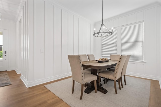 dining room with a decorative wall, a notable chandelier, light wood-type flooring, and ornamental molding