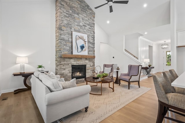 living room with stairway, light wood-type flooring, ceiling fan with notable chandelier, a fireplace, and high vaulted ceiling