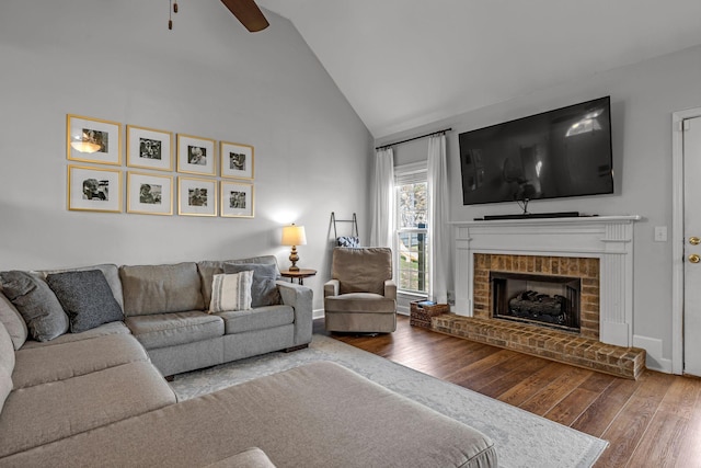 living area with high vaulted ceiling, a brick fireplace, ceiling fan, and hardwood / wood-style flooring