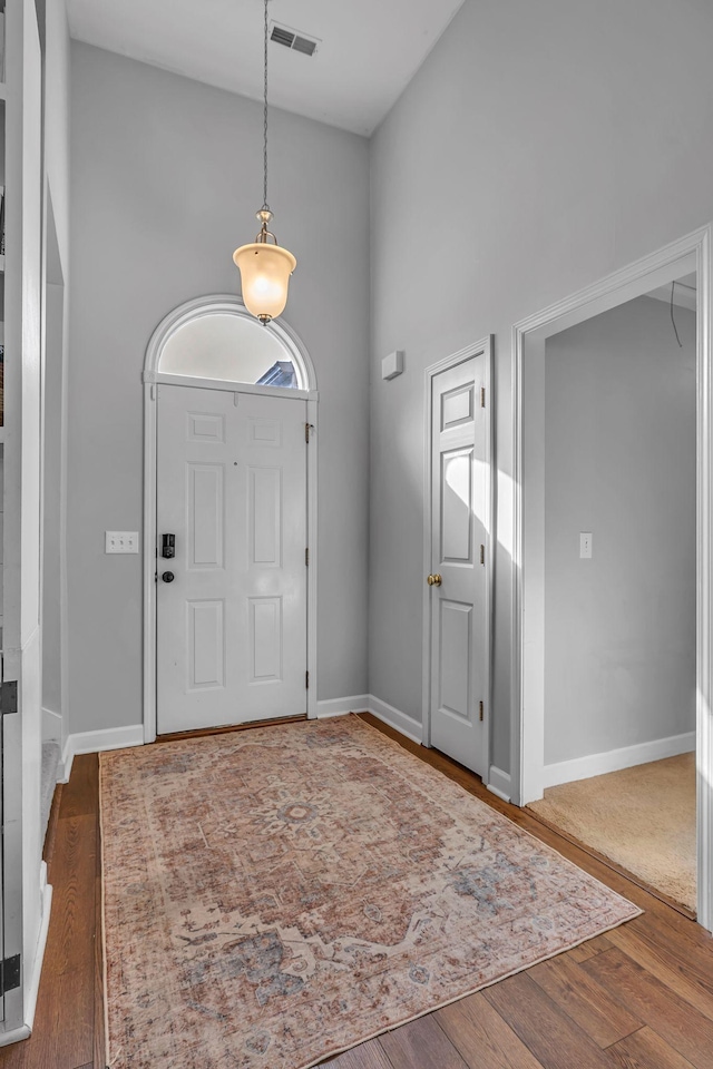 foyer entrance featuring wood finished floors, visible vents, a towering ceiling, and baseboards