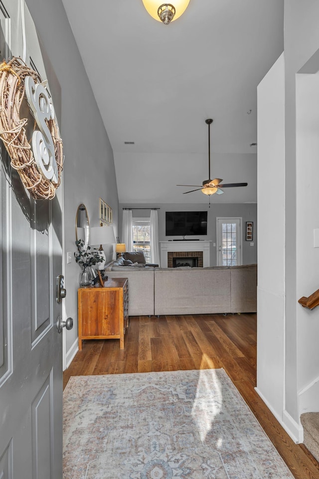 living room with wood finished floors, a fireplace, baseboards, ceiling fan, and vaulted ceiling