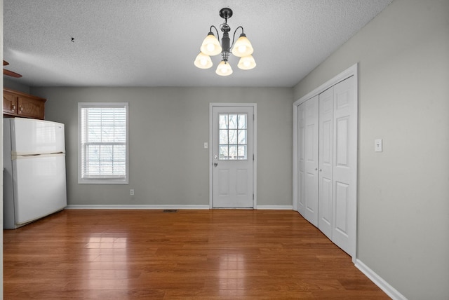 entryway with baseboards, a textured ceiling, an inviting chandelier, and wood finished floors