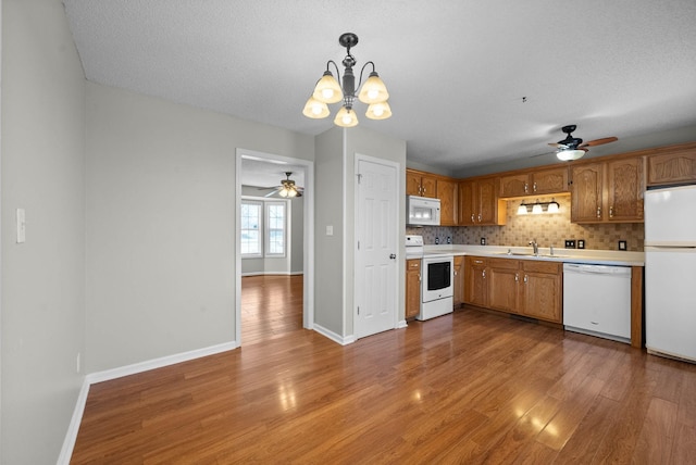 kitchen featuring light wood finished floors, light countertops, decorative backsplash, ceiling fan with notable chandelier, and white appliances