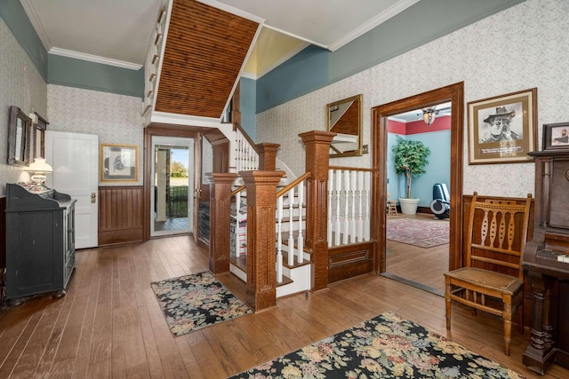 foyer entrance featuring ornamental molding, wood-type flooring, stairs, and wallpapered walls