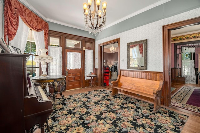 foyer featuring wood finished floors, a notable chandelier, ornamental molding, and wallpapered walls