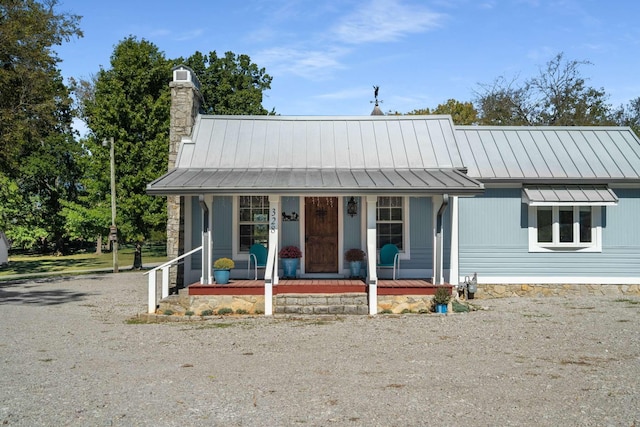 view of front of house with a standing seam roof, a chimney, covered porch, and metal roof