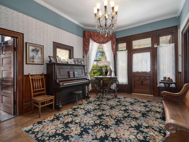 foyer featuring a notable chandelier, wood finished floors, crown molding, and wallpapered walls