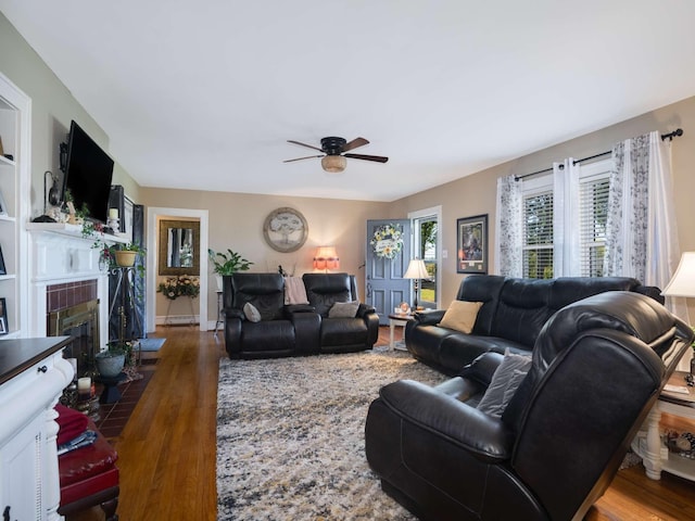 living room with baseboards, ceiling fan, a tiled fireplace, baseboard heating, and wood finished floors