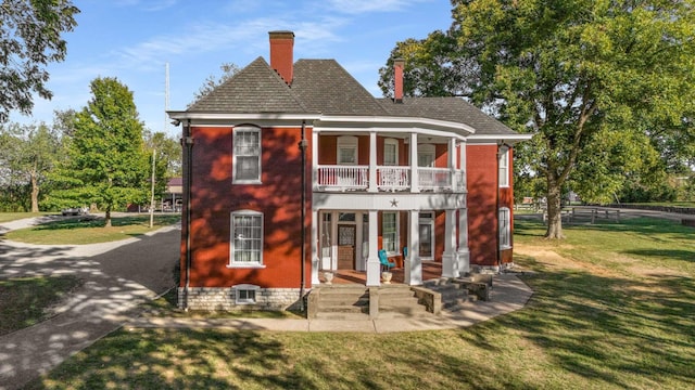 back of property featuring a balcony, fence, a porch, a chimney, and a lawn