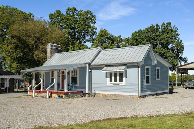 view of front of property with covered porch, a chimney, gravel driveway, and metal roof