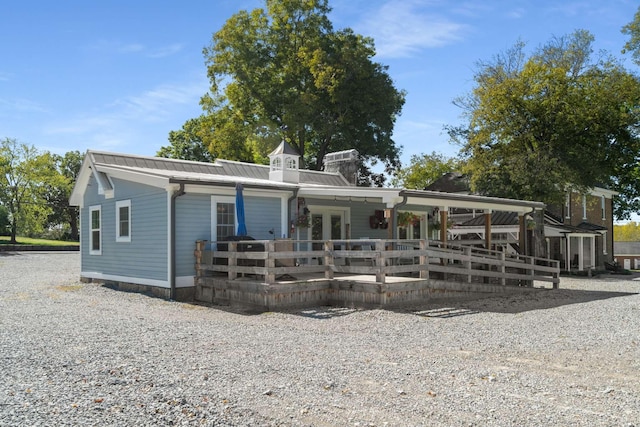 view of front of home featuring a deck, driveway, french doors, metal roof, and a chimney