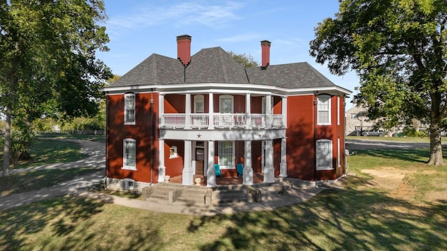 rear view of house featuring a porch, a balcony, a lawn, and a chimney