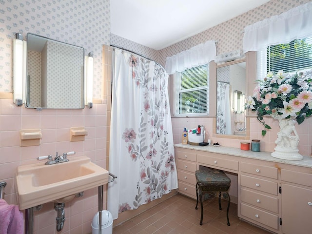 bathroom featuring wallpapered walls, a sink, curtained shower, tile walls, and tile patterned floors