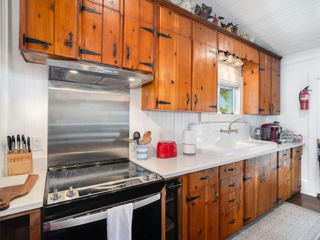 kitchen with under cabinet range hood, a sink, stainless steel electric range, brown cabinetry, and light countertops