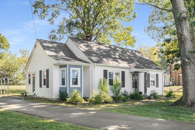 view of front of home featuring aphalt driveway, a chimney, a front yard, and a shingled roof