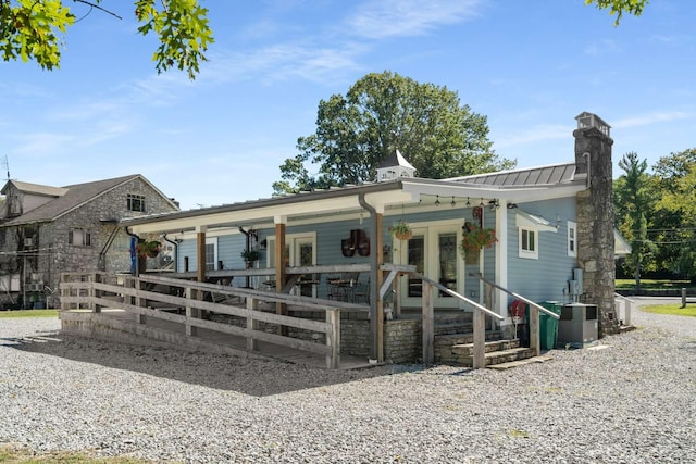 view of front of house featuring a porch, central AC unit, a chimney, metal roof, and a standing seam roof