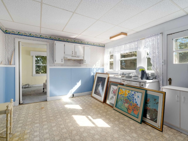 interior space with under cabinet range hood, a wainscoted wall, plenty of natural light, and wallpapered walls