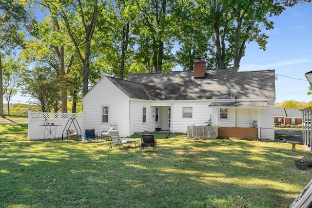 back of property with a chimney, roof with shingles, a yard, and fence