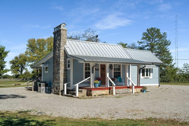 view of front of home featuring a standing seam roof, covered porch, a chimney, central air condition unit, and metal roof