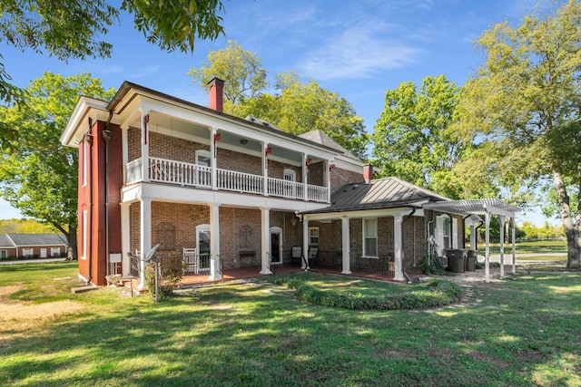back of house featuring brick siding, a lawn, a balcony, and a pergola