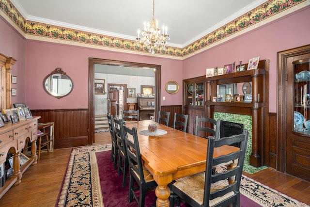 dining space with wainscoting, crown molding, an inviting chandelier, and wood finished floors