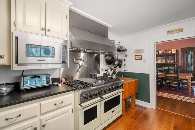kitchen with stainless steel microwave, ornamental molding, dark countertops, wood-type flooring, and range with two ovens