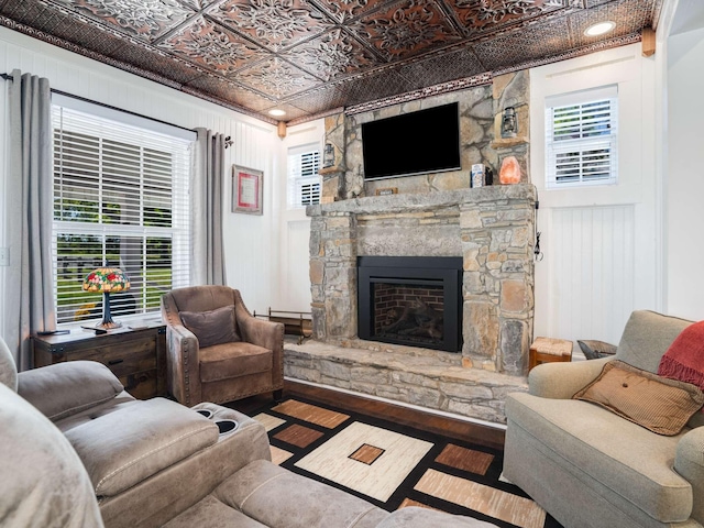 living area with a stone fireplace, plenty of natural light, wood finished floors, and an ornate ceiling