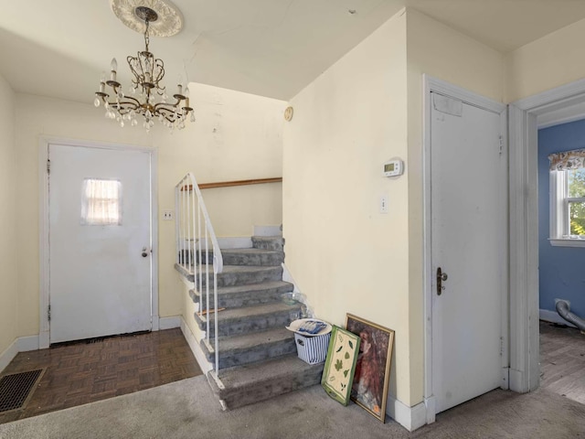 foyer entrance with stairway, baseboards, visible vents, and a chandelier