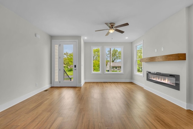 unfurnished living room featuring ceiling fan, baseboards, a glass covered fireplace, and wood finished floors