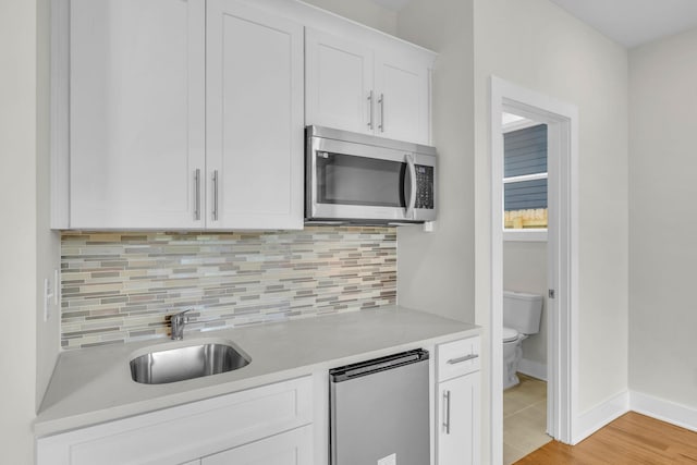 kitchen featuring light countertops, decorative backsplash, stainless steel appliances, white cabinetry, and a sink