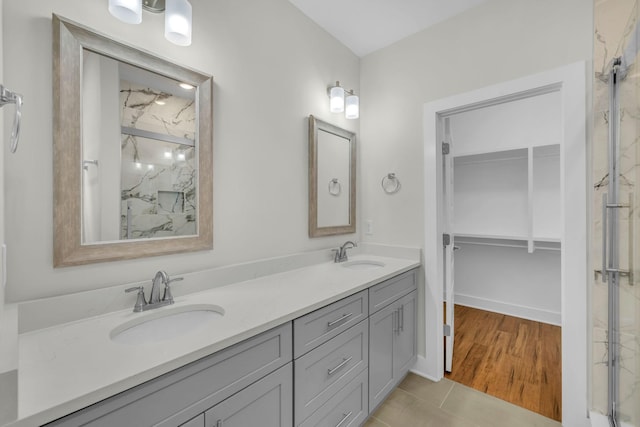 bathroom featuring a sink, a marble finish shower, and double vanity