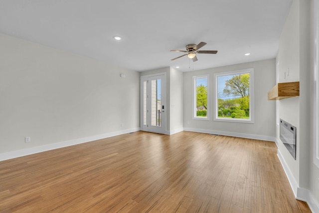 unfurnished living room featuring heating unit, a glass covered fireplace, light wood finished floors, baseboards, and ceiling fan