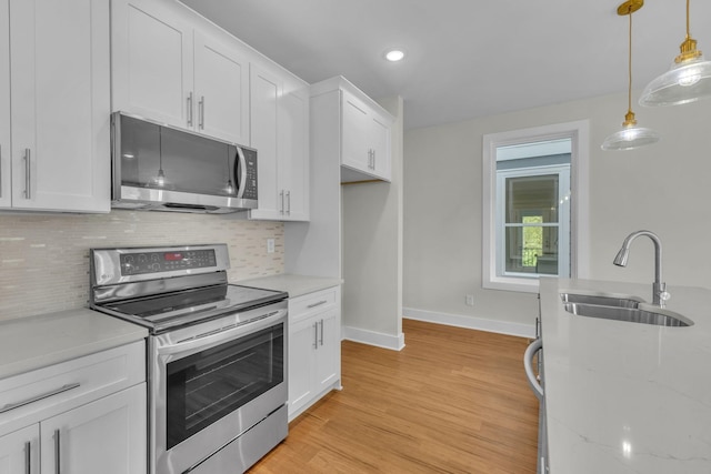 kitchen featuring a sink, tasteful backsplash, white cabinetry, stainless steel appliances, and light wood-style floors