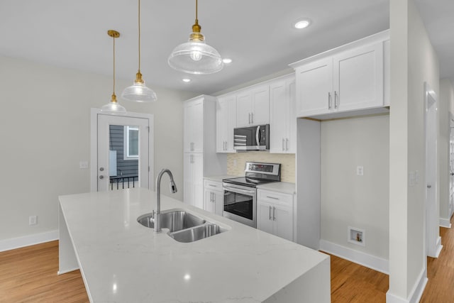 kitchen featuring a center island with sink, appliances with stainless steel finishes, light wood-style floors, and a sink