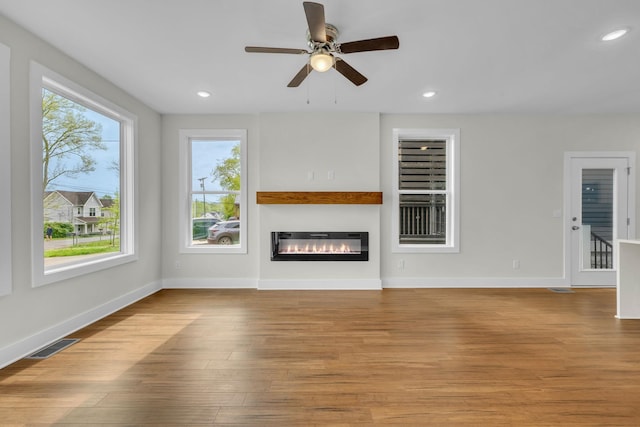 unfurnished living room featuring a glass covered fireplace, recessed lighting, wood finished floors, and visible vents