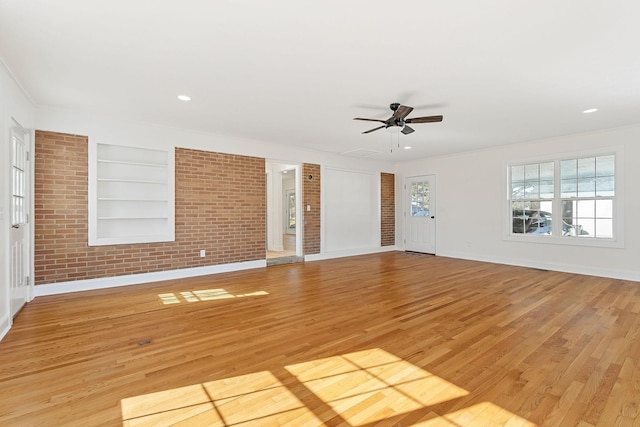 unfurnished living room featuring light wood finished floors, built in shelves, brick wall, baseboards, and ceiling fan