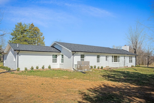 back of house featuring central air condition unit, a yard, brick siding, and a chimney