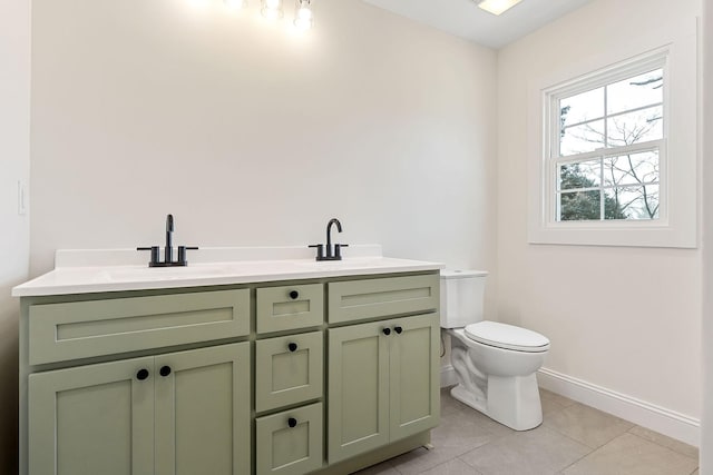 bathroom featuring baseboards, double vanity, a sink, tile patterned flooring, and toilet