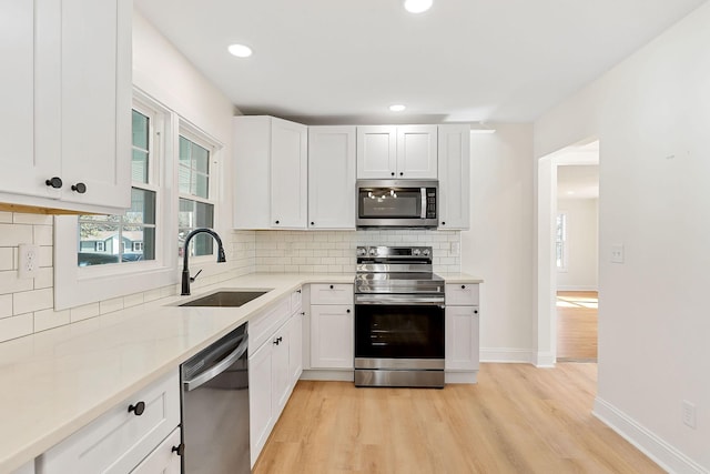 kitchen featuring appliances with stainless steel finishes, white cabinetry, light wood-type flooring, and a sink