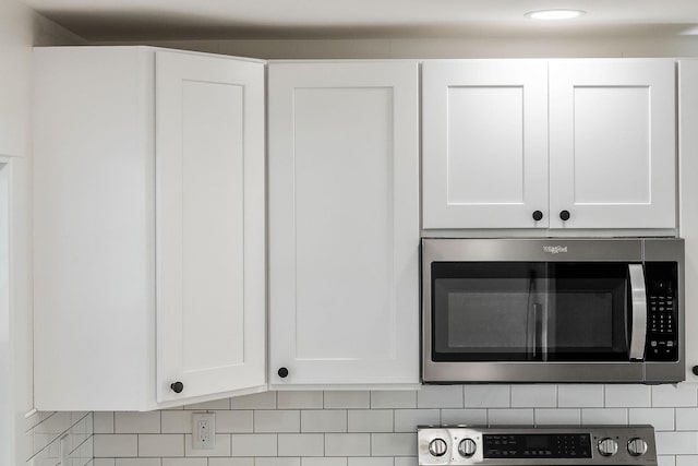 interior details with stainless steel microwave, white cabinets, range, and decorative backsplash