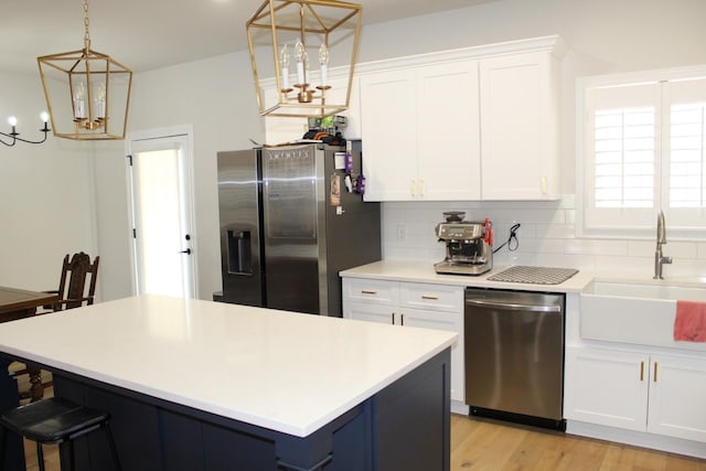 kitchen with decorative backsplash, appliances with stainless steel finishes, a notable chandelier, white cabinets, and a sink