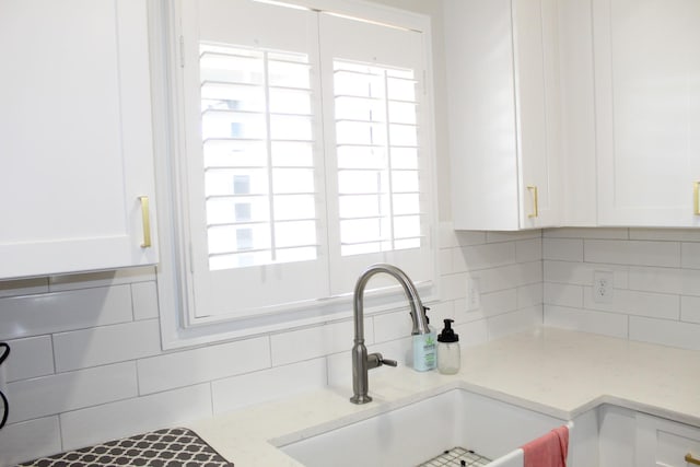 interior details with a sink, decorative backsplash, light stone countertops, and white cabinets