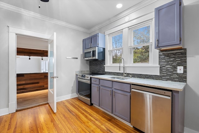 kitchen with a sink, appliances with stainless steel finishes, crown molding, light wood-type flooring, and backsplash