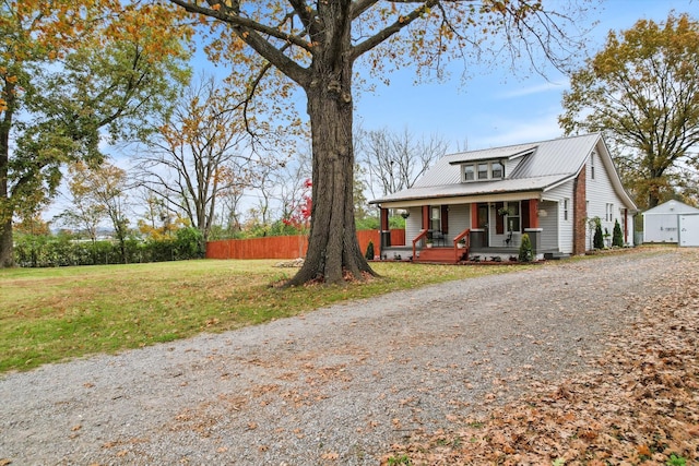 view of front of home with gravel driveway, a front lawn, fence, a porch, and metal roof